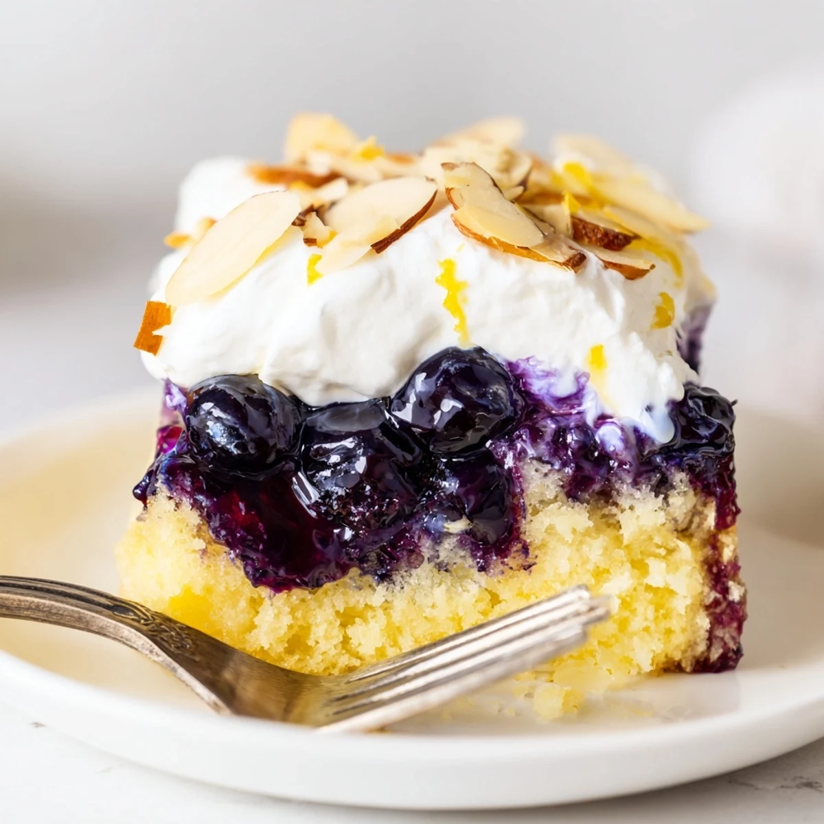 A moist Lemon Blueberry Poke Cake With Almond Topping, bursting with blueberry sauce
