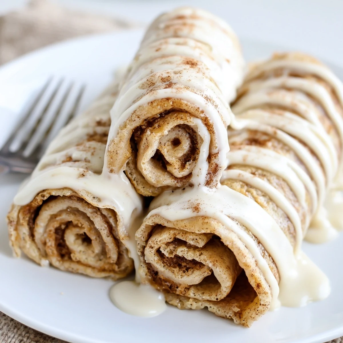 Golden cinnamon roll protein crepes drizzled with creamy vanilla glaze on a white plate.