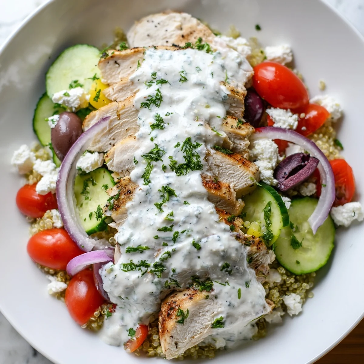 Tender Greek chicken grain bowl topped with fresh tomatoes, olives, and creamy tzatziki sauce