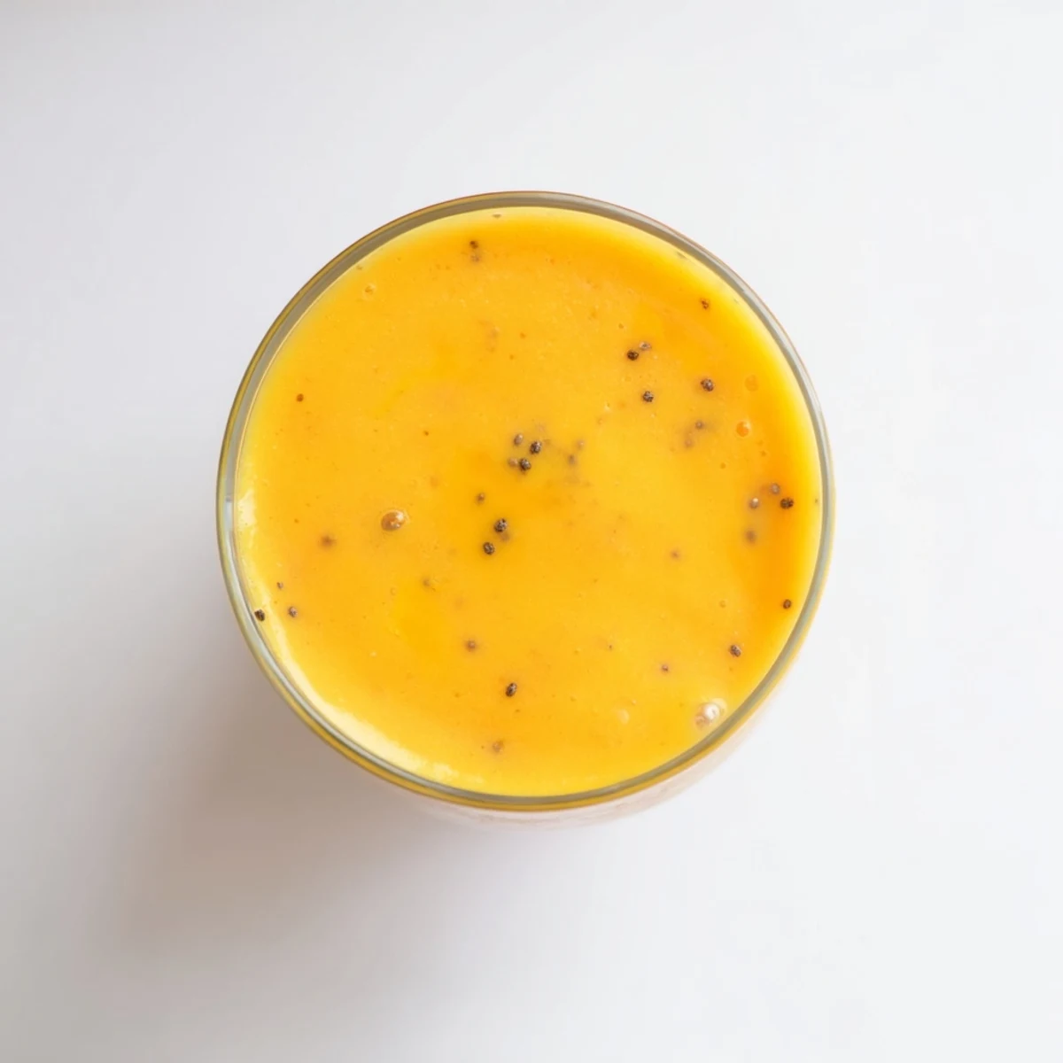 Tropical Sunrise Protein Smoothie featuring layers of bright orange mango pineapple blend topped with fresh fruit garnish in a clear glass showing creamy texture