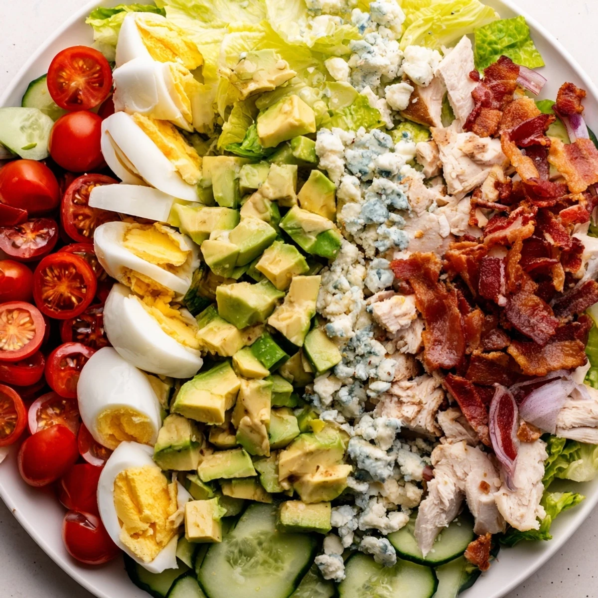 Colorful Cobb salad with tender grilled chicken, crispy bacon, and ripe avocado rows arranged on fresh romaine lettuce.