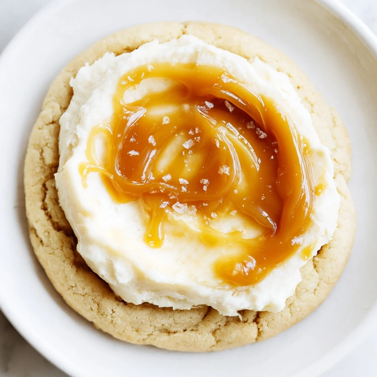 Creamy caramel cheesecake cookies topped with swirled caramel on a white dessert plate