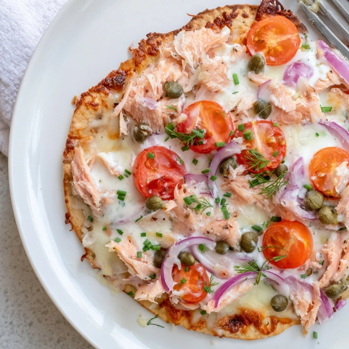 Golden baked salmon tortilla pizza topped with cherry tomatoes, capers, and red onion