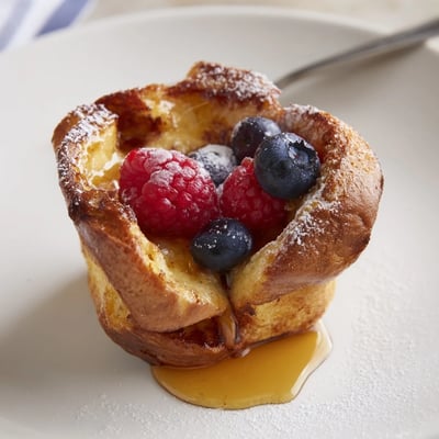 Individual Baked French Toast Cups topped with fresh berries and maple syrup