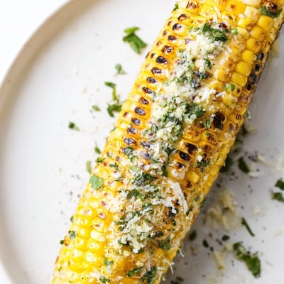 Sizzling Garlic Parmesan Corn On The Cob served with lemon wedge and parsley